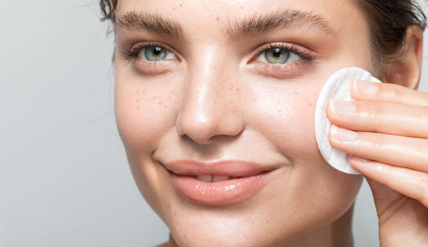 A woman wipes a cotton pad across her cheek